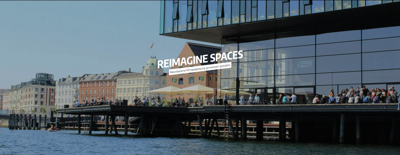Gebäude mit großer Terrasse voller Menschen, am Wasser
